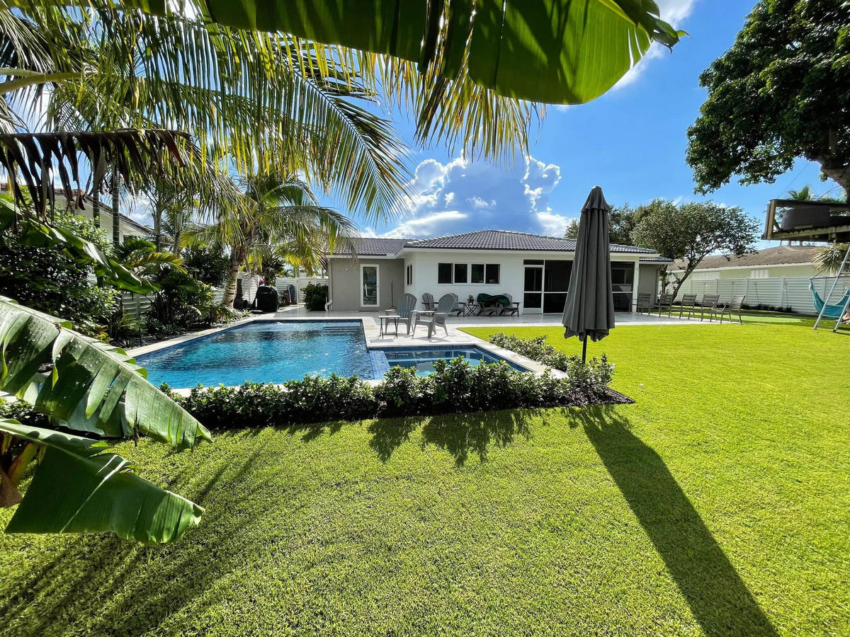 Professional landscape maintenance at a Boca Raton residential home with brick driveway and lush plantings